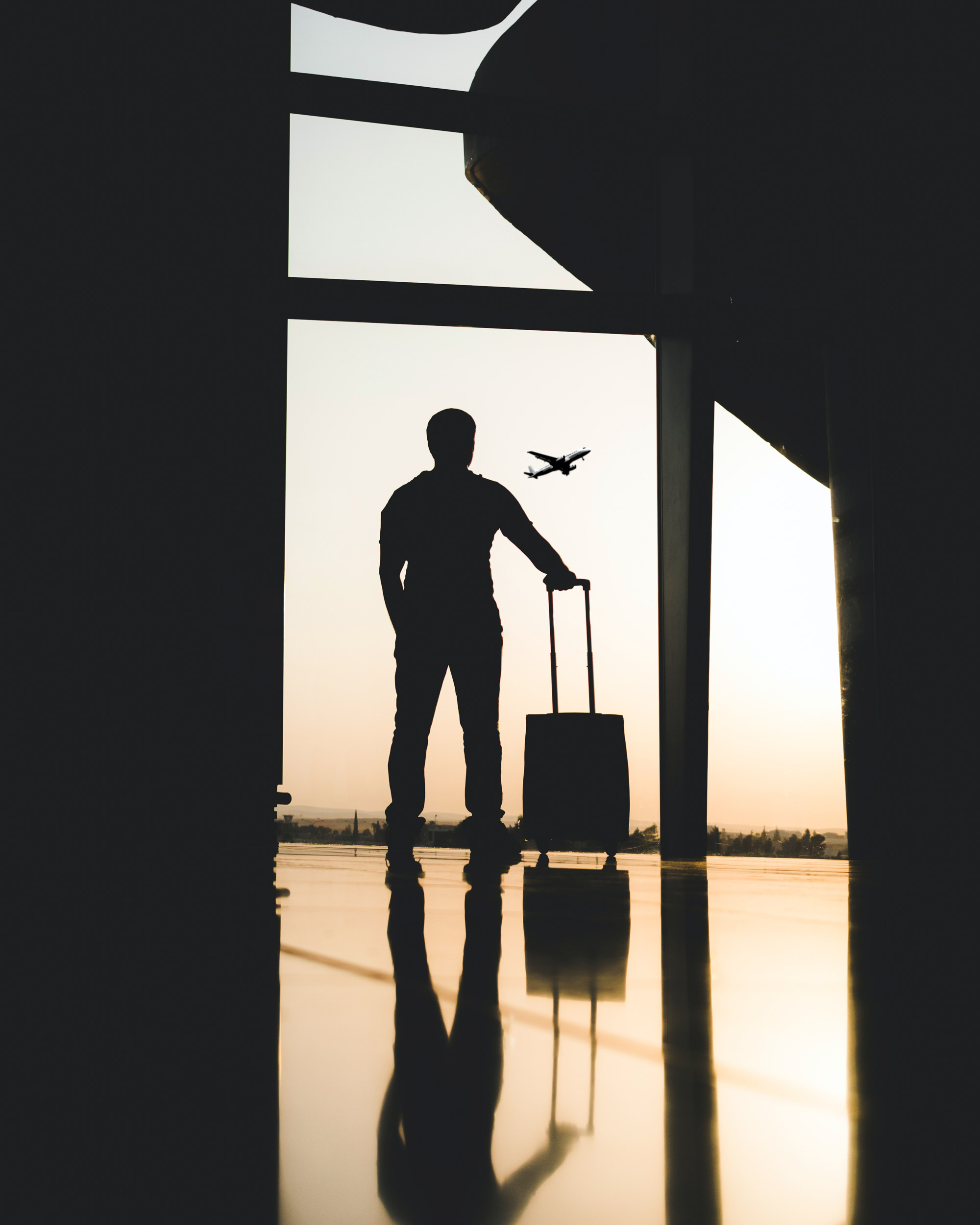 Silhouette of man with suitcase watching plane take off out window